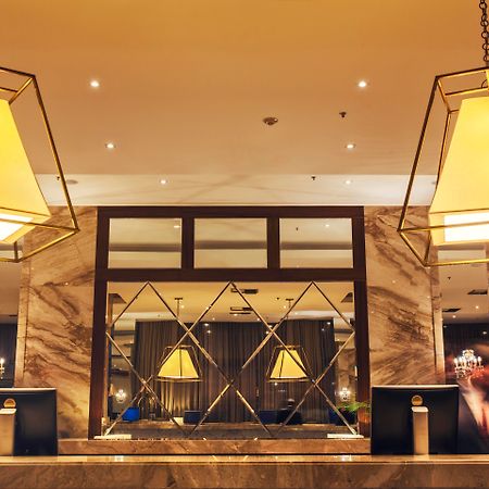 Windsor Marapendi Hotel Rio de Janeiro Exterior foto The photo shows a hotel lobby or reception area. There are large geometric light fixtures hanging from the ceiling, providing a warm glow to the space. The reception desk is made of a polished material, likely marble, with decorative elements and two