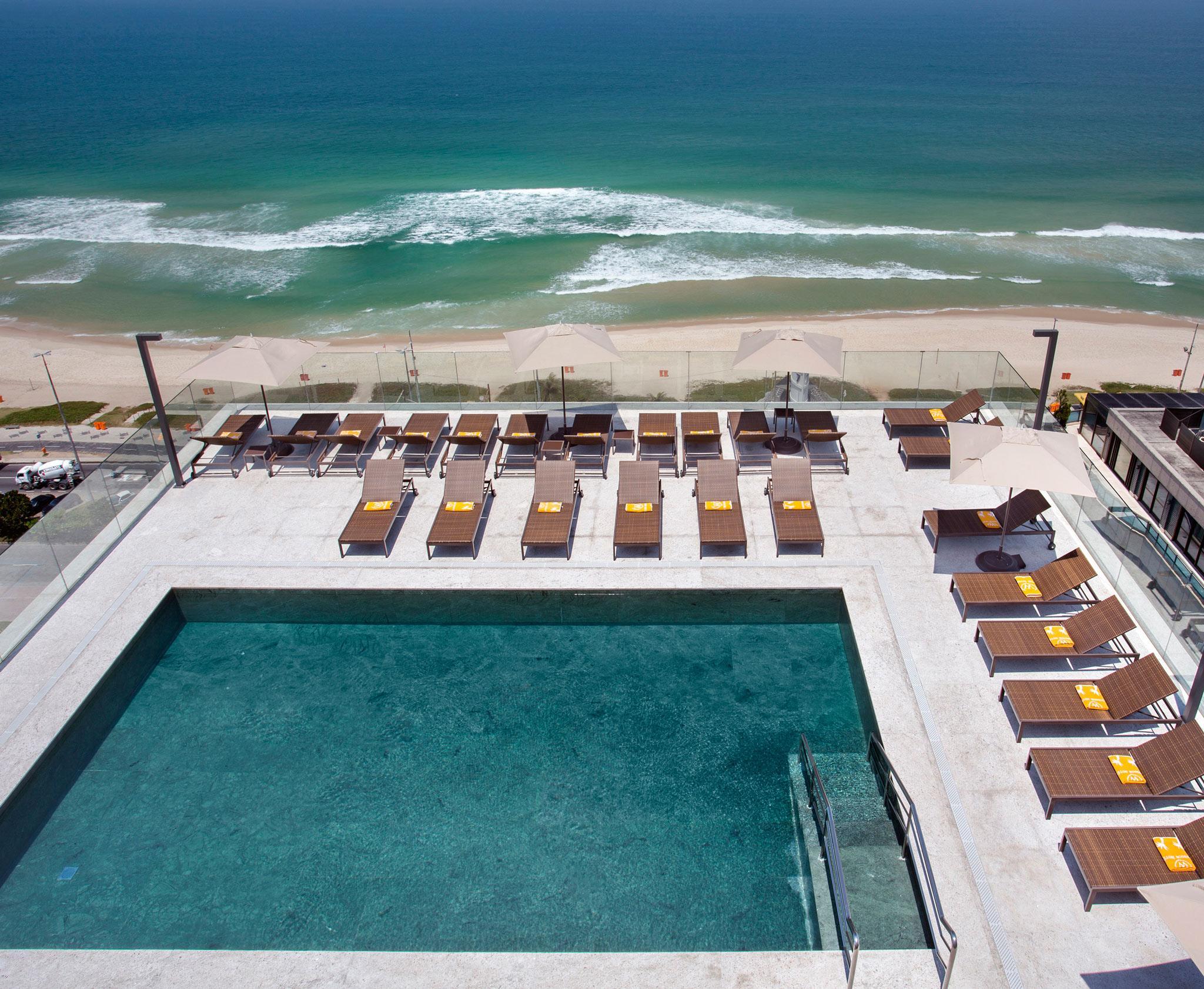 Windsor Marapendi Hotel Rio de Janeiro Exterior foto The photo shows a rooftop area with a swimming pool and several lounge chairs arranged around it. The pool has a clear blue surface, and the lounge chairs are positioned in a neat row, some with yellow cushions. In the background, you can see a beaut