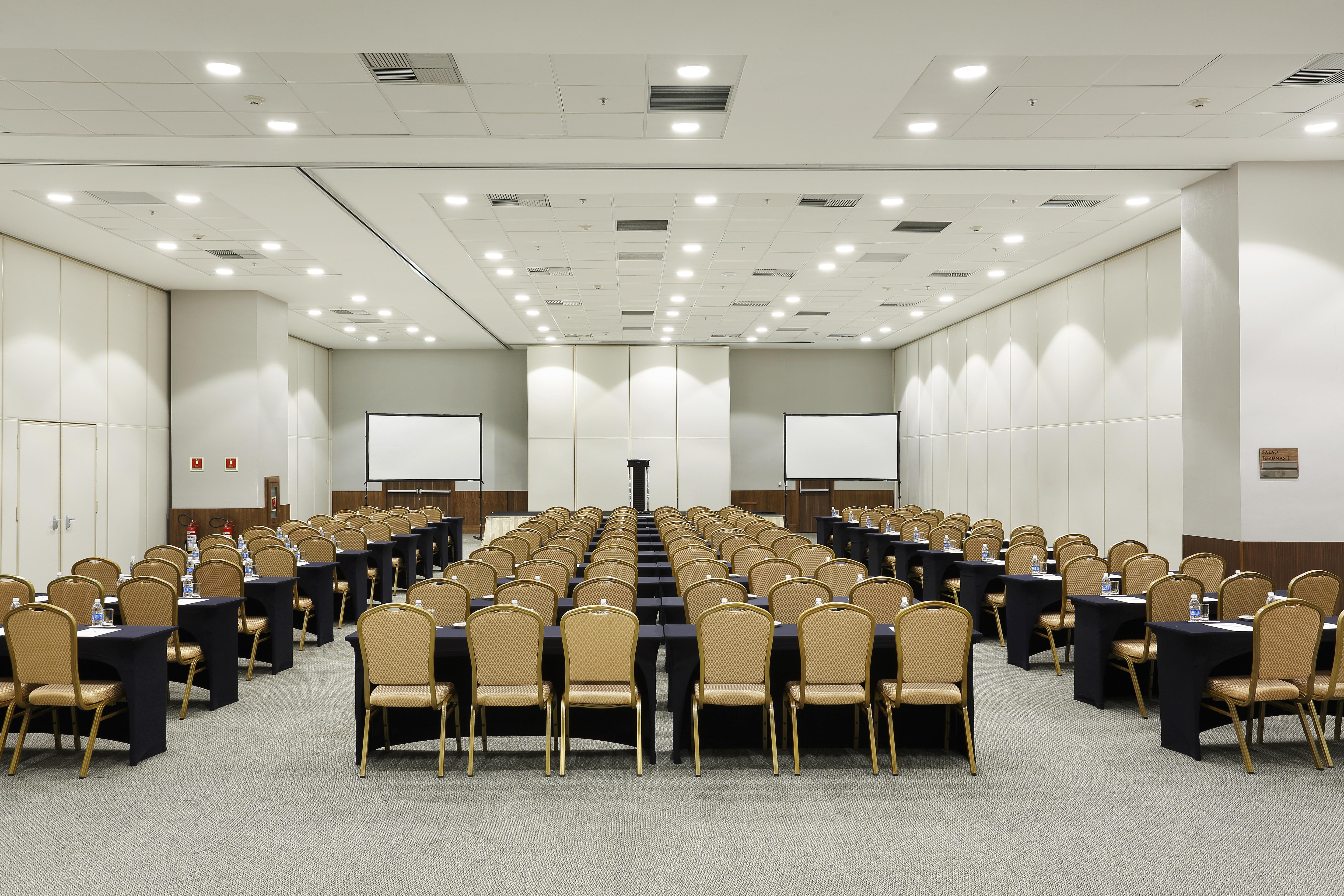 Windsor Marapendi Hotel Rio de Janeiro Exterior foto The photo shows a conference room arranged for an event or meeting. There are rows of neatly arranged chairs with golden frames, paired with black tables. The room has bright overhead lighting and features two blank screens in the front, likely for p